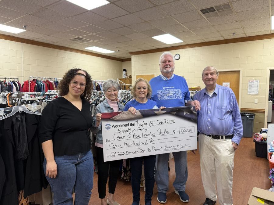 Five people stand together holding an oversized check. The check is made out to Center of Hope Homeless Shelter in the amount of $400. Behind the people are racks of donated clothing.