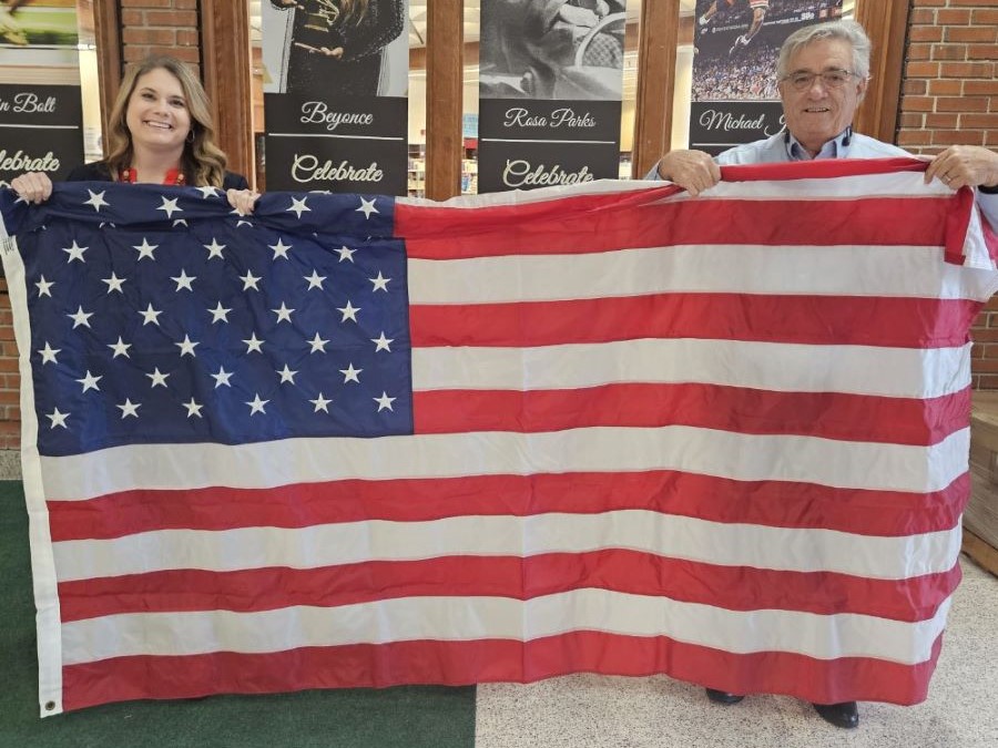 A woman and a man stand on either side of an American flag, holding it up.