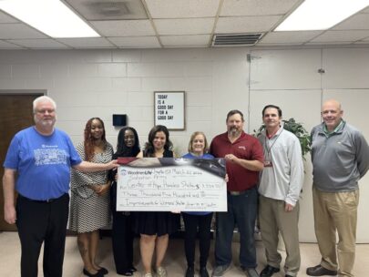 Eight people stand together holding an oversized check. The WoodmenLife-branded check is made out to Salvation Army Center of Hope Homeless Shelter in the amount of $3,500. On the wall behind the group is a sign that says "Today is a good day for a good day."