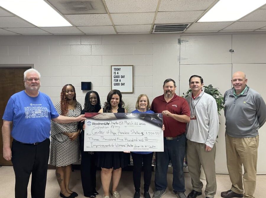 Eight people stand together holding an oversized check. The WoodmenLife-branded check is made out to Salvation Army Center of Hope Homeless Shelter in the amount of $3,500. On the wall behind the group is a sign that says "Today is a good day for a good day."