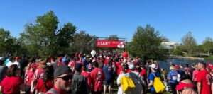 Photo is looking over a large group of people's heads and toward a red sign indicating the starting line of the Heart & Stroke Walk.