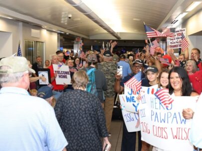 A crowd of people line a hallway, waving American flags and holding "Welcome Home" signs as people returning from the Honor Flight pass.