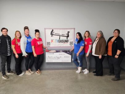 Eight people stand together for a photo. The two people at the center are holding an oversized WoodmenLife-branded check. The check is made out to Bound For a New Playground in the amount of $10,000.