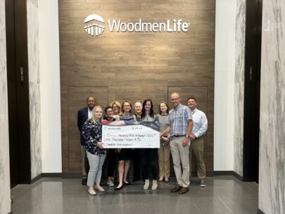 10 people pose with an oversized check showing a $1,000 donation to the Eastern Nebraska Office on Aging for its Meals on Wheels program. Behind them is the WoodmenLife logo on the wall.