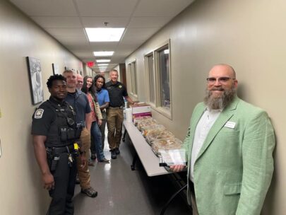 A WoodmenLife Sales Representative holds a small, glass award. He is standing in a hallway alongside several members of the DeSoto County Sheriff's Office, some of whom are in uniform.