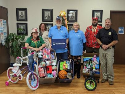 Six people, standing in front of a Christmas tree, pose with boxes of toys and kids bikes.