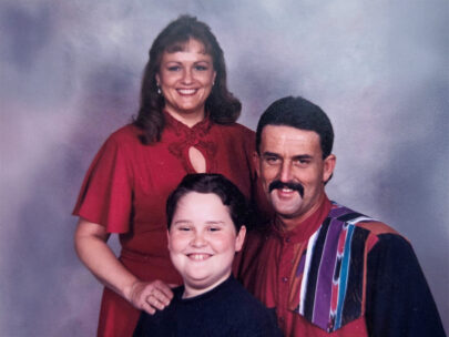 Image is a posed family photo, with a woman standing, a man seated, and a young boy seated in front.