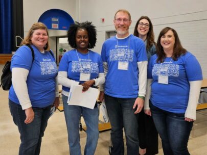 Five WoodmenLife associates, all wearing matching blue T-shirts, are pictured. They are volunteering at an Omaha school as part of WoodmenLife's work with Partnership 4 Kids.