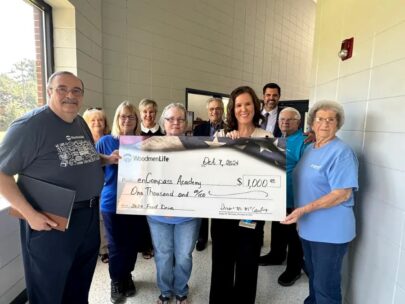 10 people stand around an oversized check. The check is made out to enCompass Academy in the amount of $1,000.