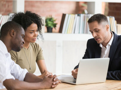 Stock image shows a man in a suit talking with a couple over a laptop.