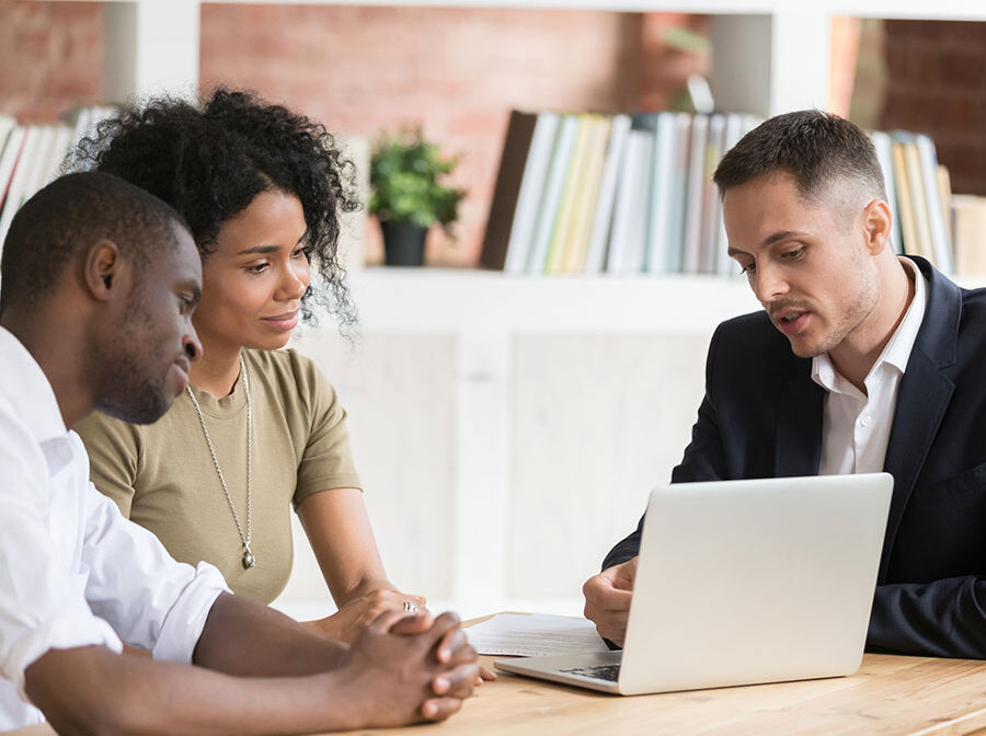 Stock image shows a man in a suit talking with a couple over a laptop.