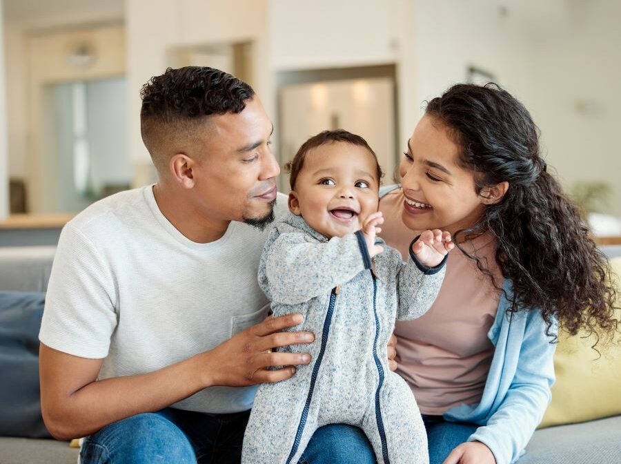 Stock photo of a young family. Mom and dad are sitting, looking at the infant between them.