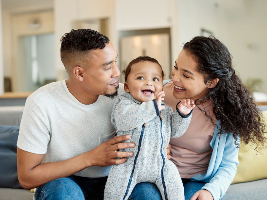 Stock photo of a young family. Mom and dad are sitting, looking at the infant between them.